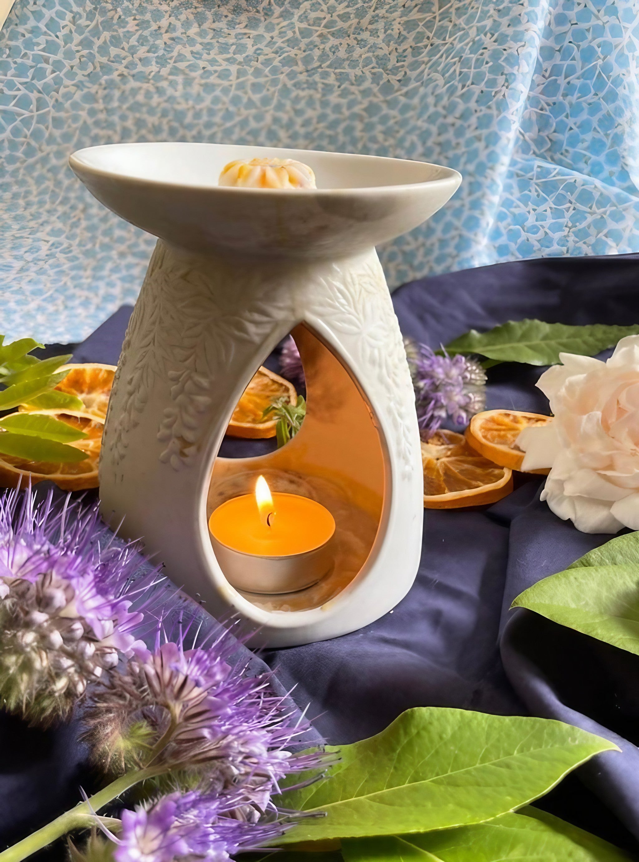 Ceramic wax melt warmer with candle, surrounded by dried citrus, flowers, and greenery, creating a cozy ambiance.