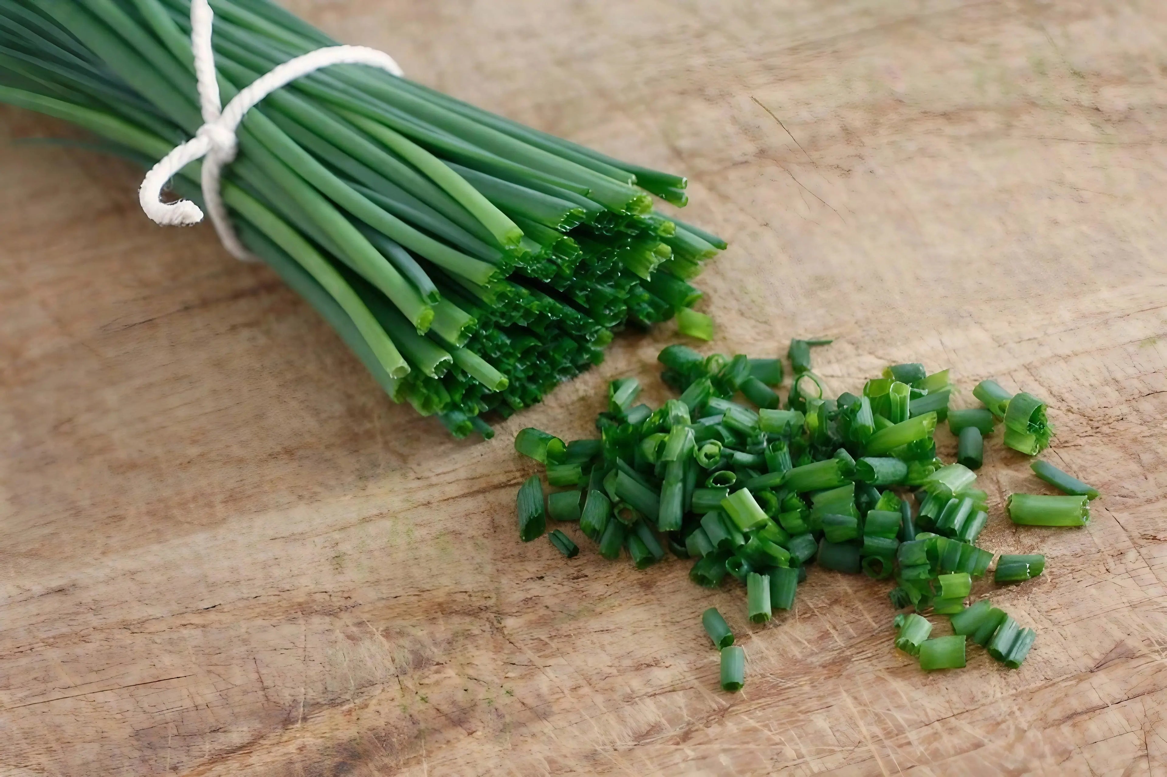 Bunch of green chives tied together with a small pile of chopped chives on a wooden surface