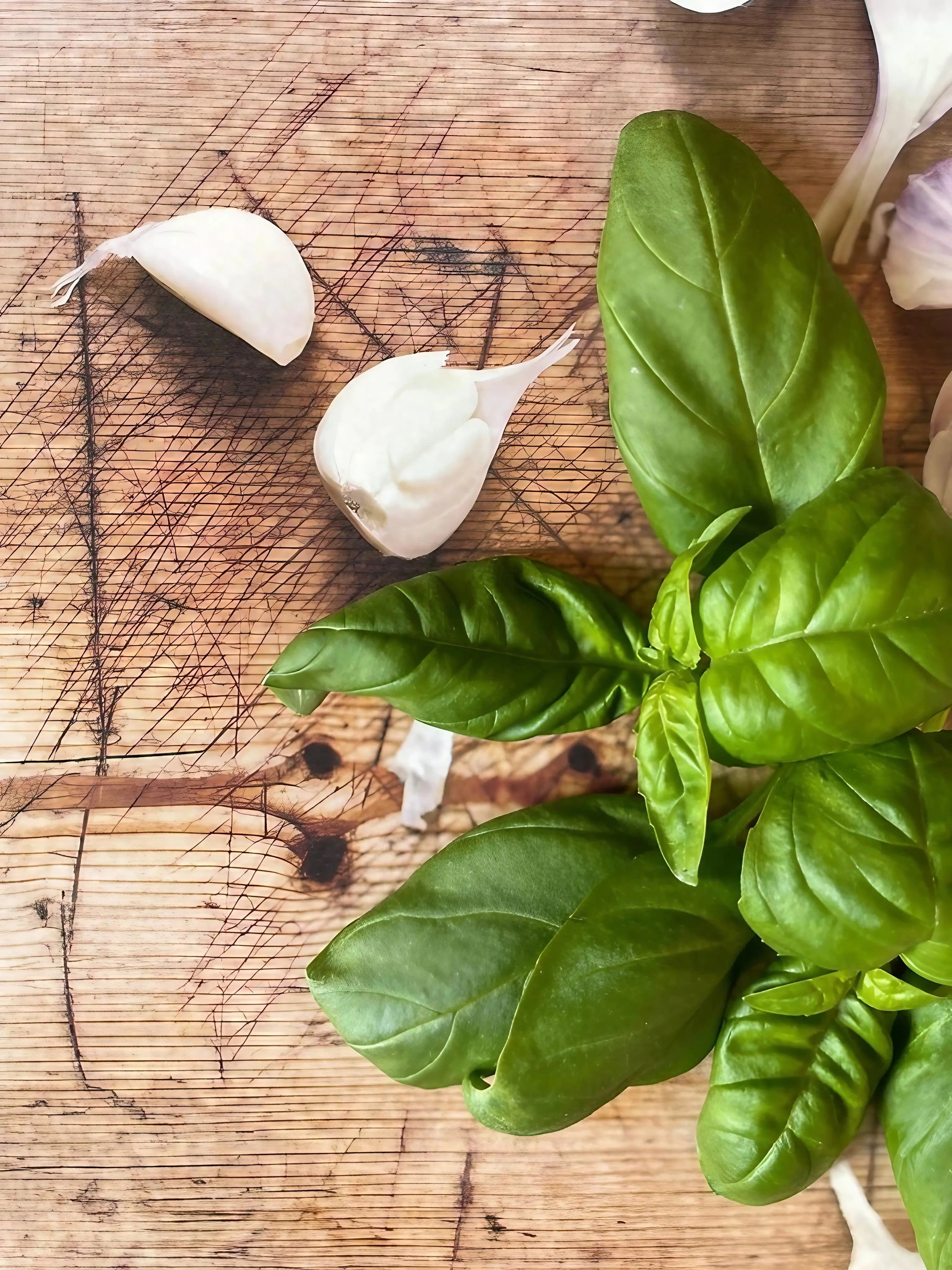 Basil leaves on a wooden cutting board with garlic bulbs
