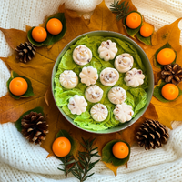 The Tadpole & Piglet Thai Lime & Mango Botanical Wax Melts, shaped like white flowers, are displayed on green leaves with autumn leaves, pinecones, orange fruits, and greenery atop a white knitted fabric.