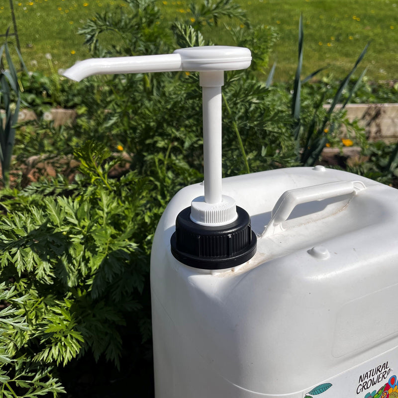 The Natural Grower Jerry Can 10 Litre Dispensing Pump, with a top handle, sits outdoors among green plants and grass—ideal for storing and applying liquid feed.