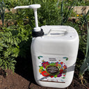 A white 10 litre Jerry Can Dispensing Pump of Natural Grower sits on garden soil among green leafy plants, displaying a colorful label with flowers and fruits.