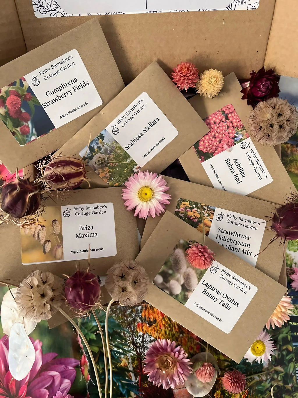 A flat lay of "Flowers to Grow - Perfect for Drying" seed packets by Bishy Barnabees Cottage Garden, surrounded by everlasting flowers in pink, purple, and cream, plus floral cards—all beautifully arranged on a wooden surface.
