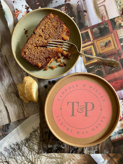 Delicious slice of gingerbread cake on a plate with Tadpole &amp; Piglet wax melts in the background, creating a cozy atmosphere.