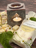 The Moroccan Arch Soapstone Wax Melt Burner by Bishy Barnabees Cottage Garden, paired with lemongrass and ginger wax melts and surrounded by chamomile flowers, creates a relaxing, spa-like atmosphere on a wooden surface.