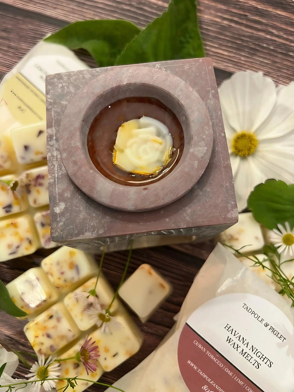 The Moroccan Arch Soapstone Wax Melt Burner by Bishy Barnabees Cottage Garden sits on wood with wax melts topped with dried flowers, green leaves, white daisies, and a bag labeled "Havana Nights Wax Melts.