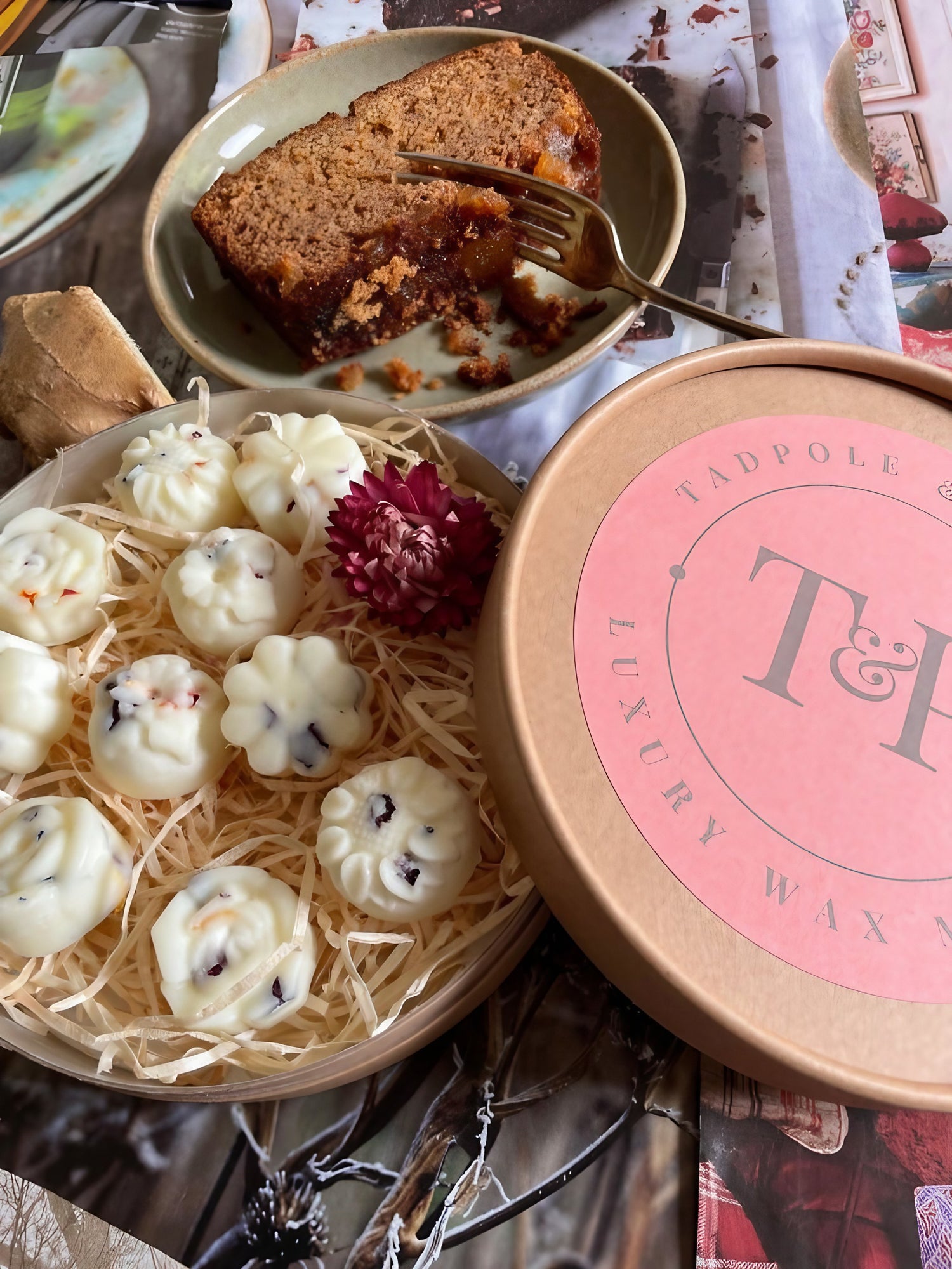 Gingerbread wax melts in a gift box next to a slice of cake on a festive table setting.