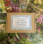 A cardboard box labeled "The Patio Flower Garden Collection" by Bishy Barnabees Cottage Garden sits atop a lively backdrop of container flower seeds and compact garden plants in full bloom.