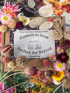 A package of Flowers to Grow - Perfect for Drying by Bishy Barnabees Cottage Garden is shown among dried and fresh blooms in pink, yellow, and cream—perfect for creating sustainable floral decor.