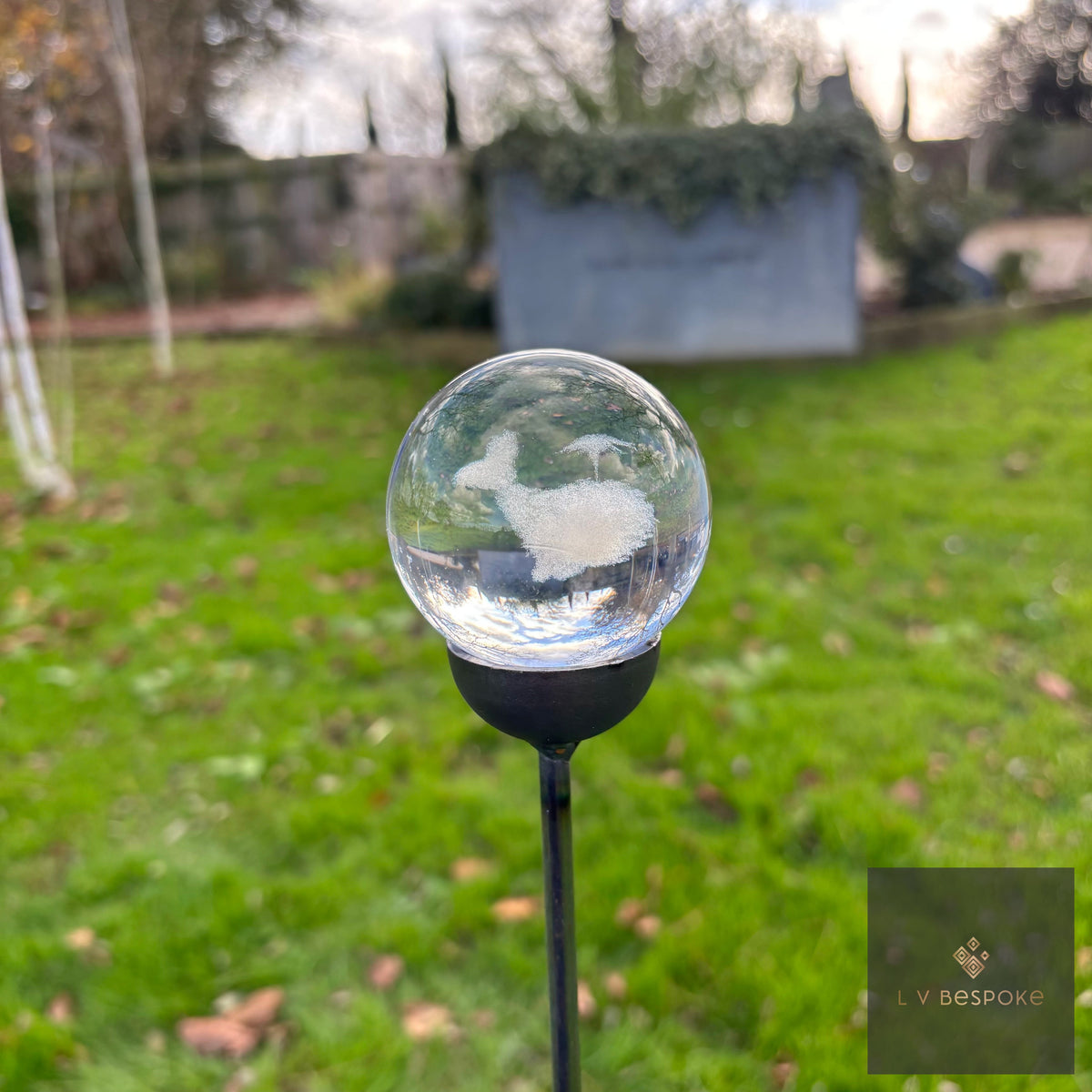 3D orb garden stake with an etched whale, lawn and shed behind