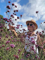 Woman in a straw hat smiling among tall Verbena bonariensis under a blue sky
