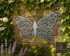 Lacy metal butterfly wall art on a garden wall among flowers