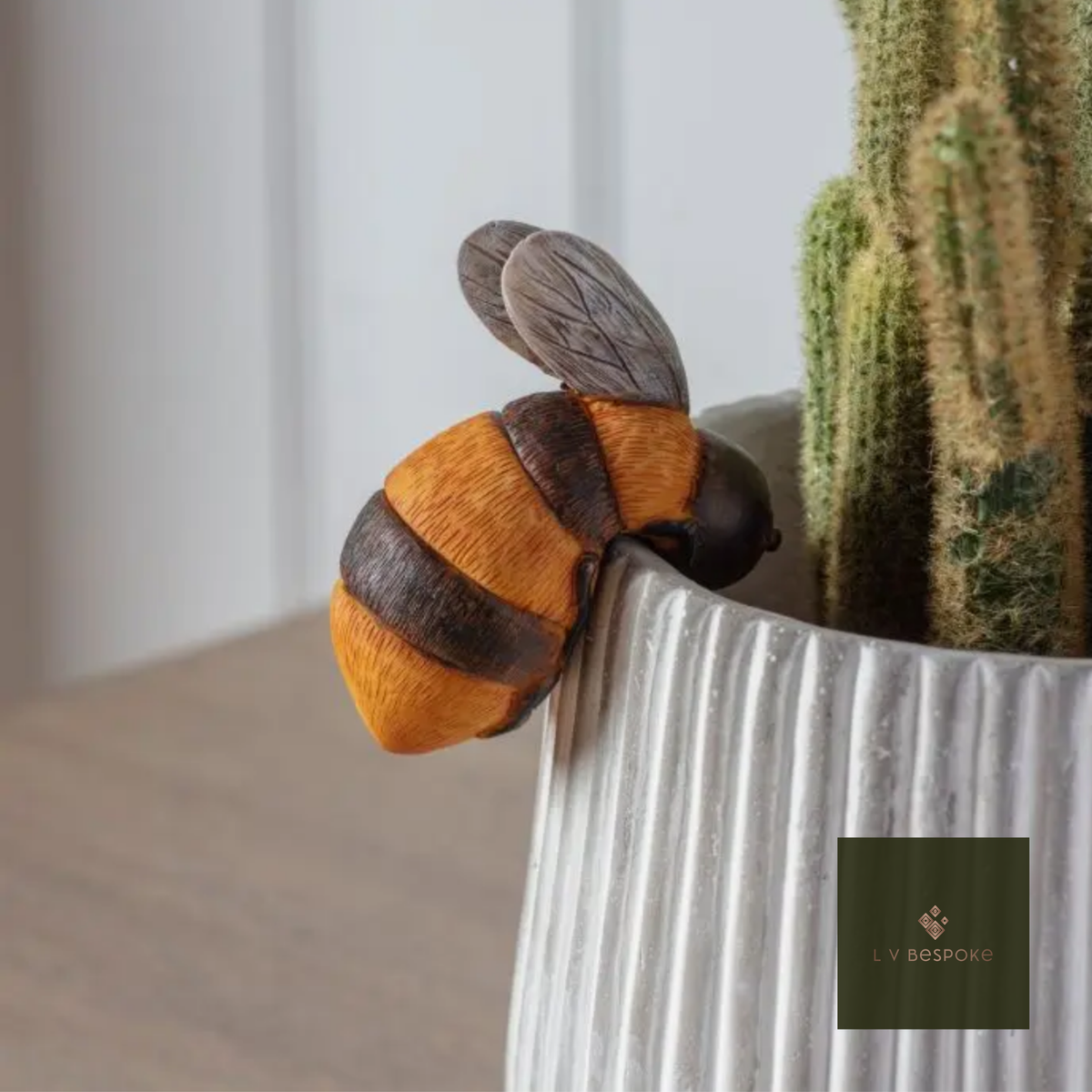 Ceramic bumblebee pot hanger on a white ribbed pot beside a cactus