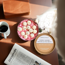 A round box of Tadpole & Piglet Coffee Caramel Botanical Wax Melts sits on a table with a cup of coffee, a brown leather wallet, and a newspaper, as soft morning light creates a cozy atmosphere.