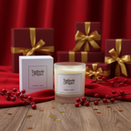 A Tadpole & Piglet Cranberry & Orange Scented Candle with a wooden wick and its box rest on red fabric amid festive berries and red gift boxes with gold ribbons, evoking a cozy holiday vibe.