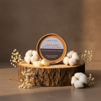 A round tin of Tadpole & Piglet’s Damson & Rose Botanical Wax Melts rests on tree bark with cotton bolls, baby’s breath, and pale yellow melts. A softly lit neutral backdrop emphasizes their fruity floral scent.