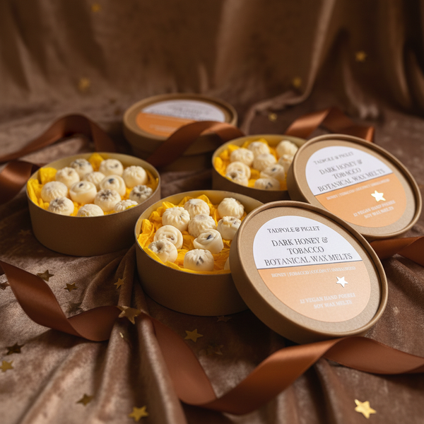 Bishy Barnabees Cottage Garden's Dark Honey & Tobacco Botanical Wax Melts are displayed in round boxes on brown velvet with star confetti and ribbon, some elegantly topped for a luxurious presentation.