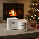 A Tadpole & Piglet Earl Grey & Cucumber scented candle and its box rest on a table before a glowing fireplace and festive Christmas tree, surrounded by ornaments and gifts, filling the scene with cozy holiday charm from natural soy wax warmth.
