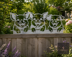 Metal three pigs wall art on a wooden fence behind flowers