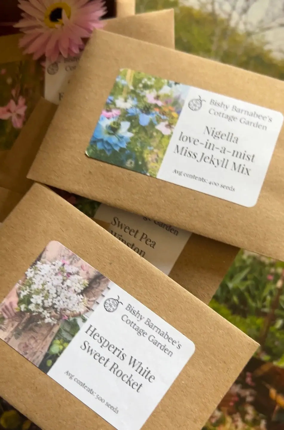 Several brown seed packets from Bishy Barnabees Cottage Garden Ltd’s "A Year in a Cottage Garden - Flower Box (12 Packs)" are shown, each with flower images—an ideal gift or addition to your own cottage garden.