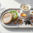 A marble tray displays Tadpole & Piglet’s Myrrh & Tonka Botanical Wax Melts, featuring flower-shaped hand-poured melts in a round box, a white wax warmer, dried flowers, myrrh resin, and tonka beans.