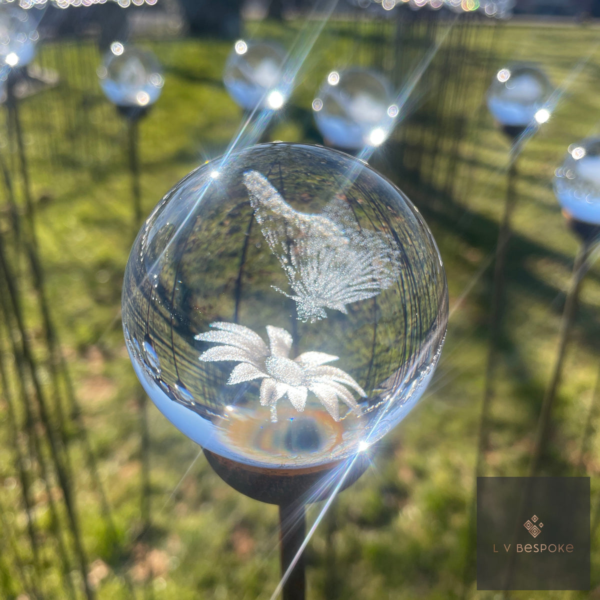 3D orb garden stake with crystal-effect sphere catching the light in a flower border