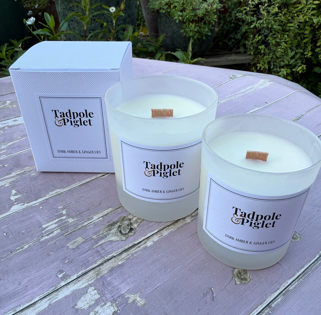 Two Tadpole Piglet candles on a wooden surface with a box in the background.