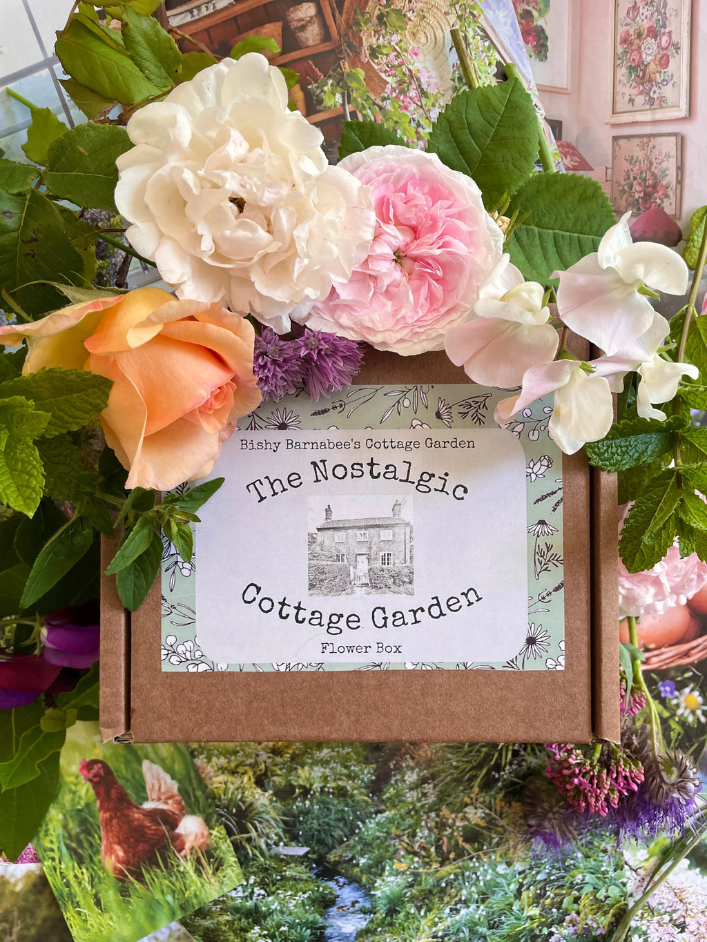 A cardboard box labeled "The Nostalgic Cottage Garden Flower Box - 24 Packets" by Bishy Barnabees Cottage Garden sits among colorful flowers, garden-themed books or cards, and cottage garden seed packets, creating a charming, floral display.