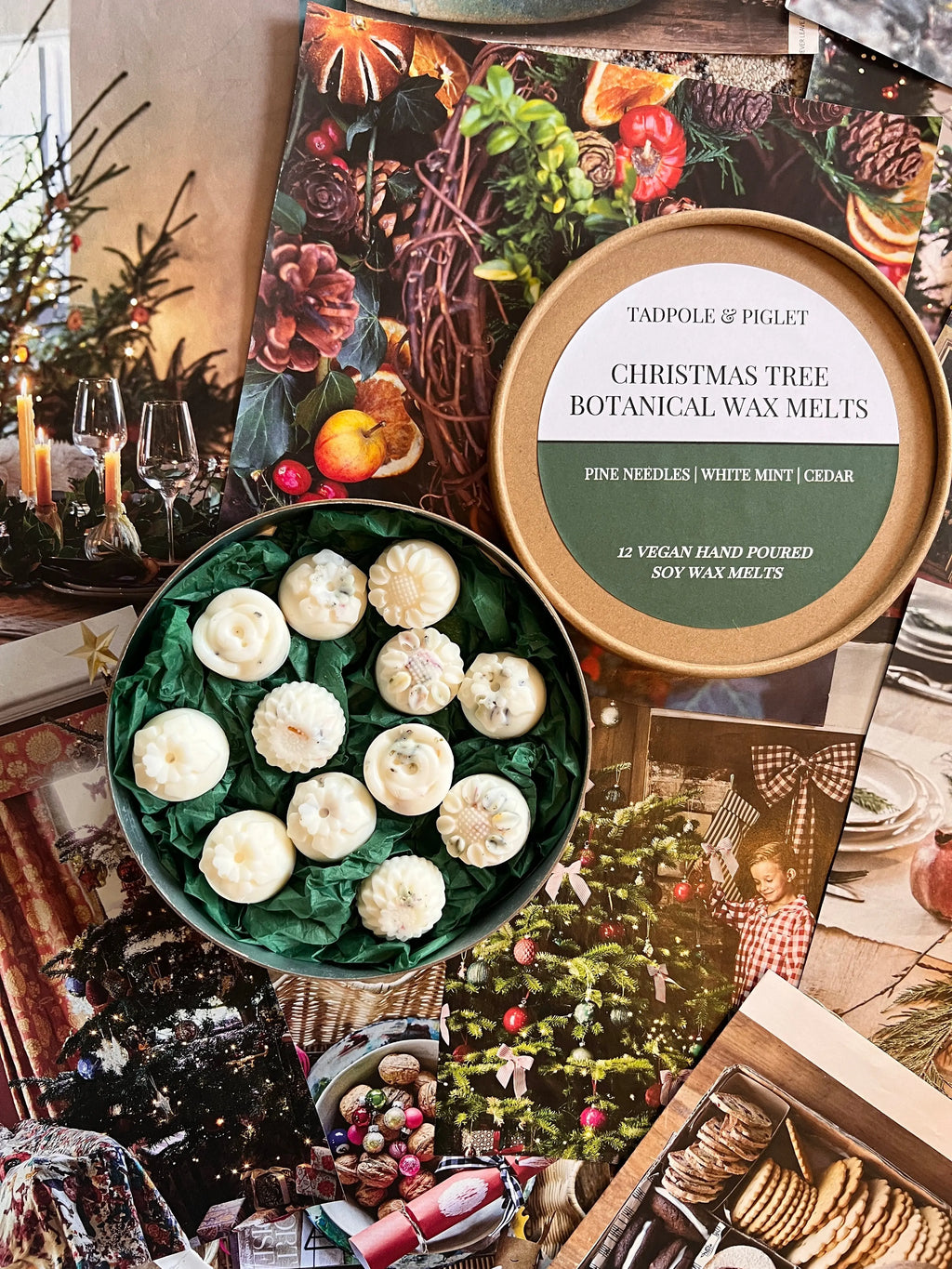 An open Tadpole & Piglet Christmas Tree Botanical Wax Melts tin rests on festive holiday images, showing 12 white Nordmann Fir wax melts arranged on green paper inside.