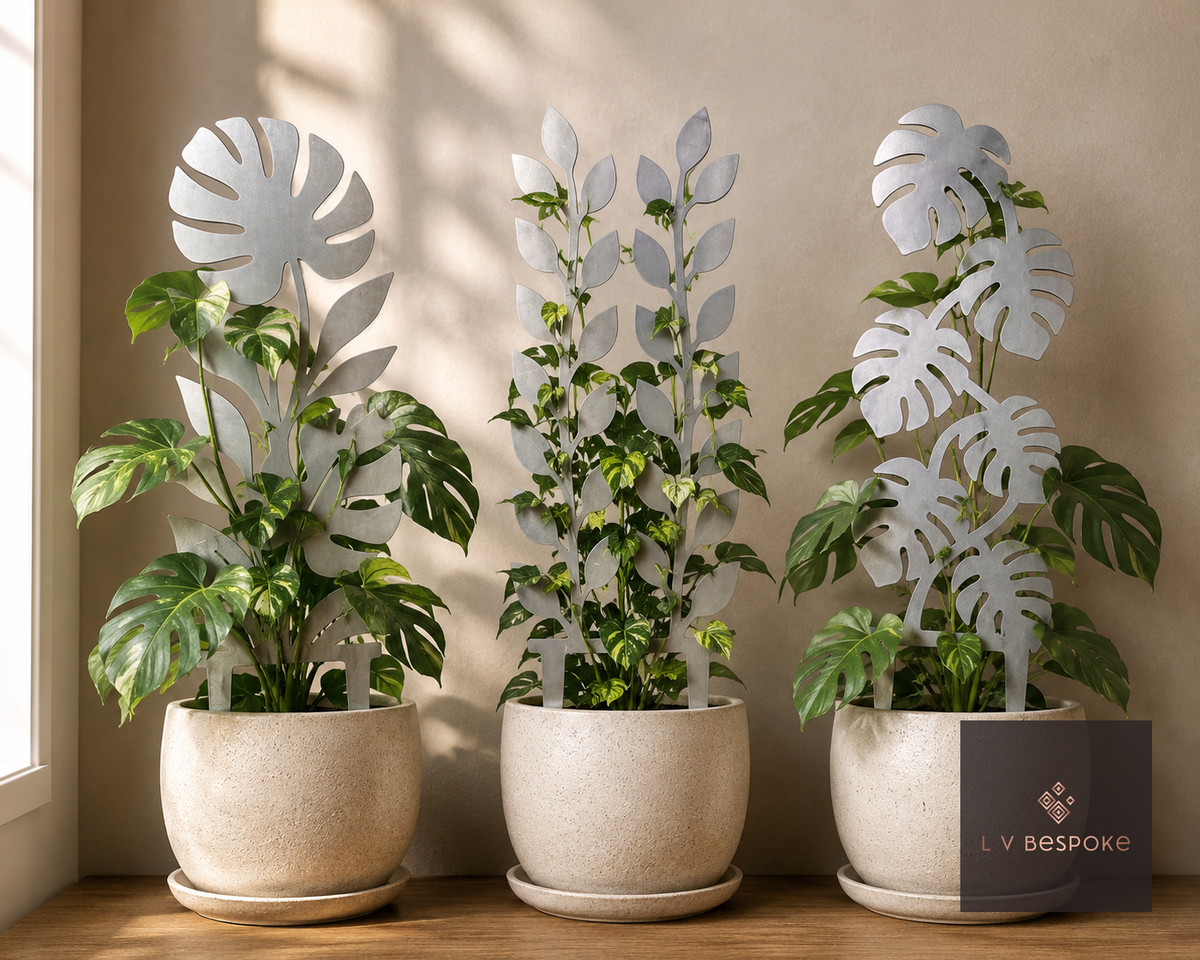 Three metal indoor plant supports with leaf designs in white pots