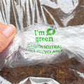 A hand holds a clear plastic bag labeled "Im green, Carbon Neutral, and 100% Recyclable" in green text, showcasing the eco-friendly packaging of Natural Plant Feed 22L "Bag in a Box" by Natural Grower with soil beneath.