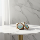 Two small round containers with kraft lids, labeled "Lemon Verbena Botanical Wax Melts" by Tadpole & Piglet, rest on a white marble table. Sunlight filters in, casting gentle shadows and highlighting their promise of fresh citrus scent.