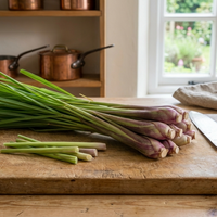 Lemon Grass East Indian by Bishy Barnabees Cottage Garden Ltd—fresh stalks on a cutting board with a kitchen knife and garden view—an ideal Thai curry herb for your recipes.