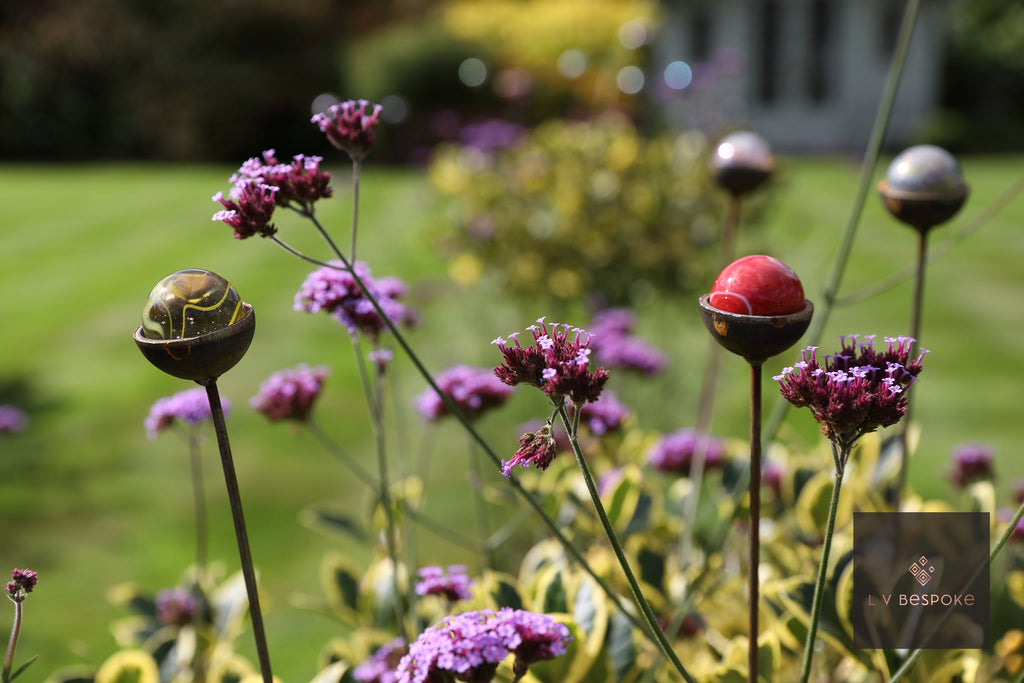 Glass marble garden stakes among purple verbena in a lawn