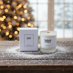 The Tadpole & Piglet Myrrh & Tonka Scented Candle, in its white box, rests on a snowy wooden table with holiday lights and a blurred Christmas tree beyond the window—an ideal touch of luxury home fragrance this season.