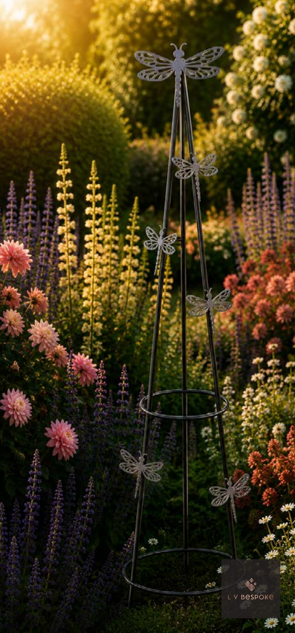 Metal dragonfly-topped obelisk in a flower border at sunset