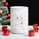 The Tadpole & Piglet White Matte Lattice Cut Wax Burner sits on faux snow with red gift boxes and a festive tree branch—an ideal minimalist touch to add fragrance and style to your holiday décor.