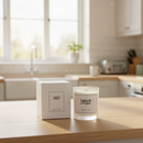 A Tadpole & Piglet Wild Fig & Cassis Scented Candle with a wooden wick sits next to its box on a kitchen counter, sunlight highlighting the clean, modern space in the background.