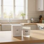 A Tadpole & Piglet Wild Fig & Cassis Scented Candle with a wooden wick sits next to its box on a kitchen counter, sunlight highlighting the clean, modern space in the background.