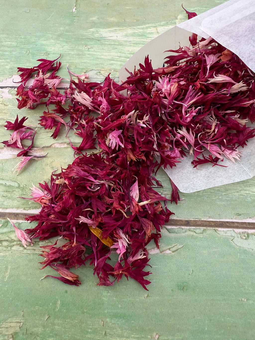 Dried Flower Petals – burgundy petals spilling from a bag onto green painted wood