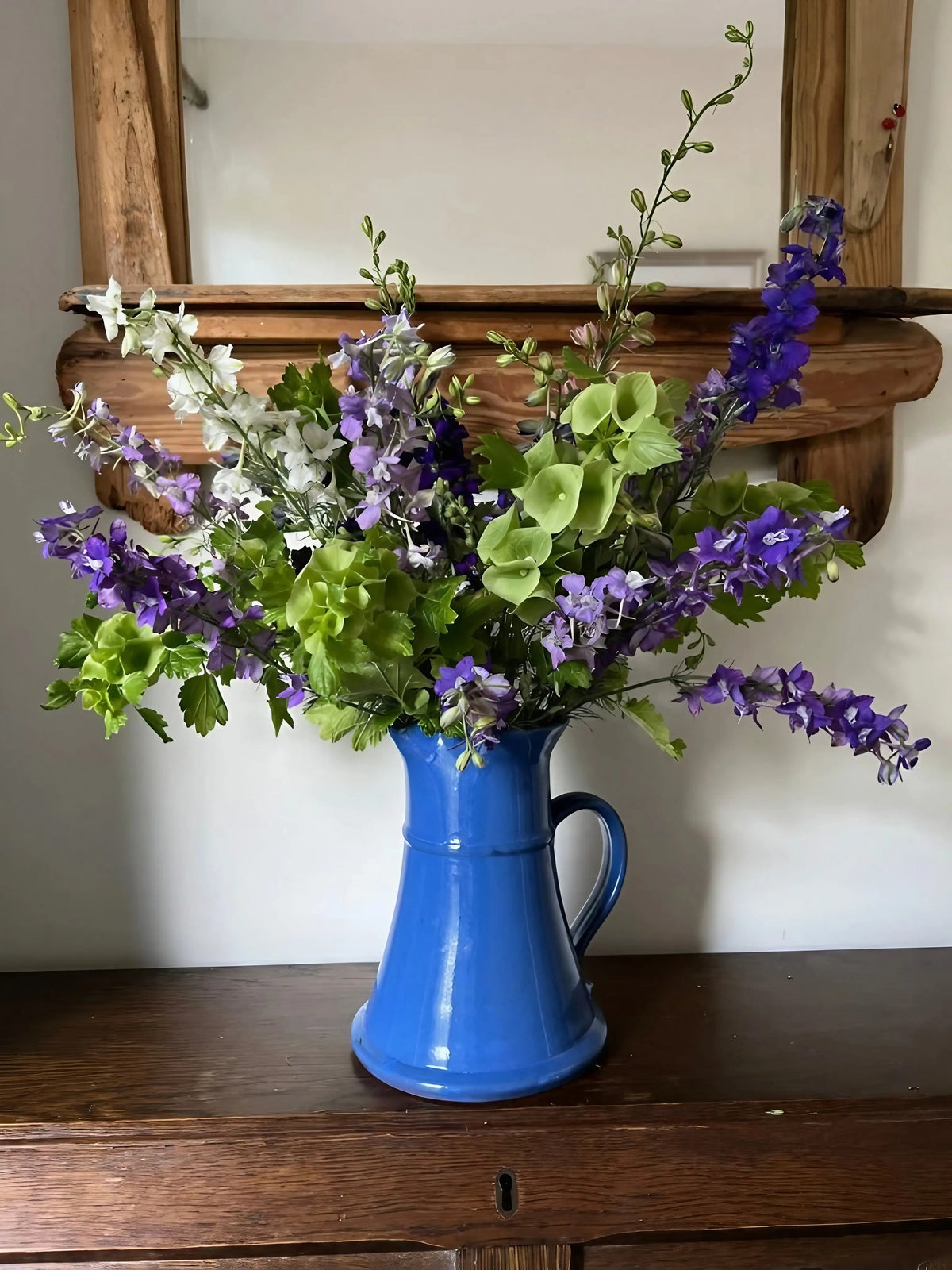 Bells of Ireland in a blue ceramic jug with purple and white flowers on a dark table