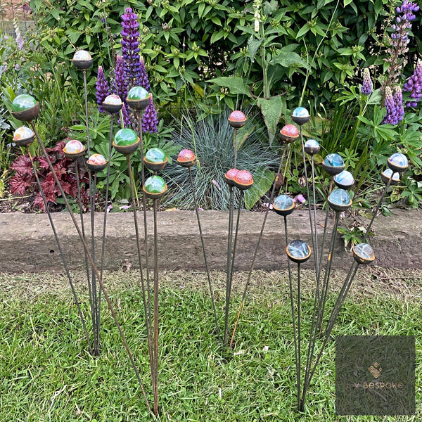 Clusters of colourful marble garden stakes splayed among lupins beside a raised bed