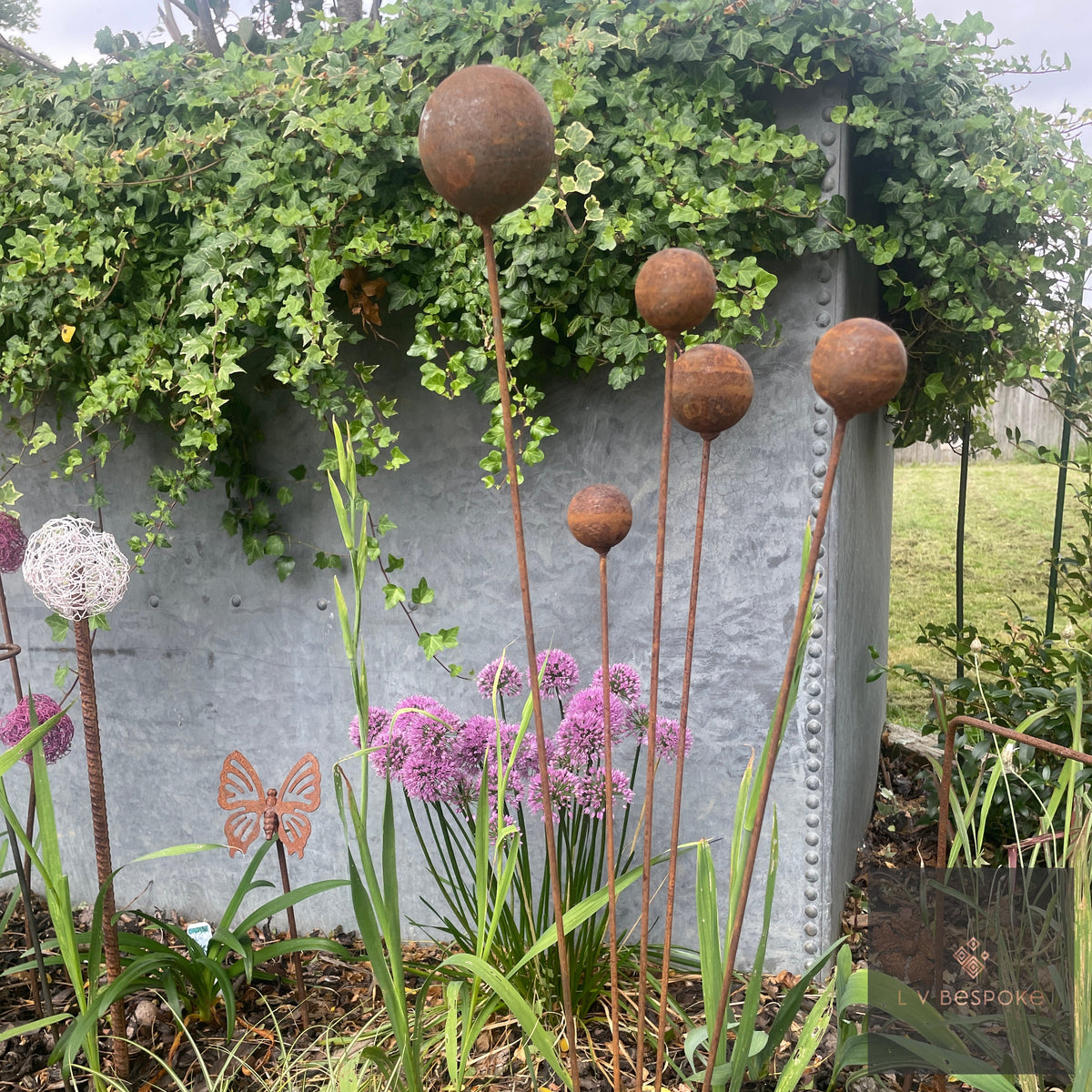 Rusty steel ball cluster above alliums against a galvanised planter