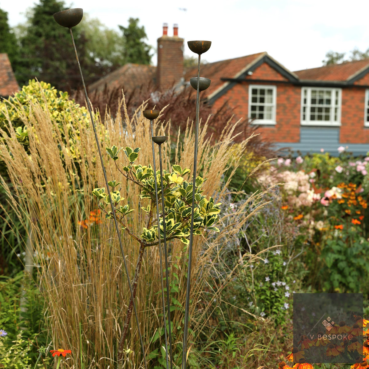 Steel ball feature among tall ornamental grasses with a red brick house behind