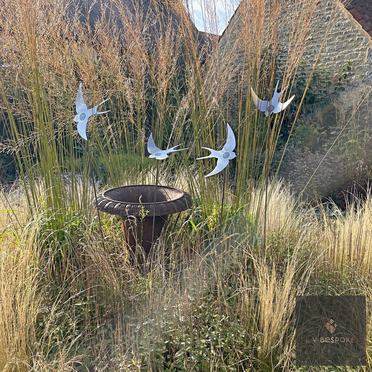 Flock of white swallow stakes flying over tall grasses and a bird bath