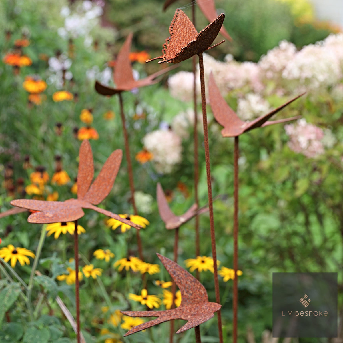 Group of rusty swallow stakes flying over yellow and orange flowers