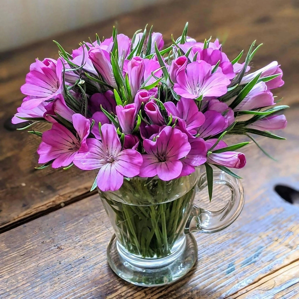 Pink Corncockle flowers in a clear glass mug on a wooden surface