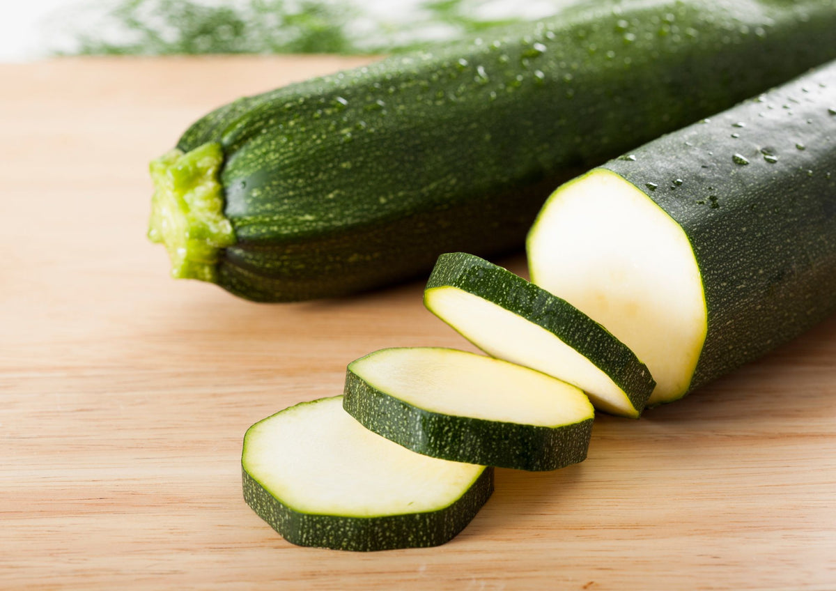 Courgette All Green Bush – dark green courgettes, one sliced, on a wooden board