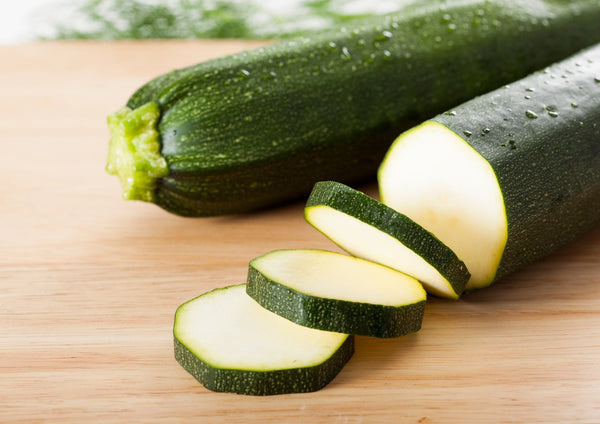 Courgette All Green Bush – dark green courgettes, one sliced, on a wooden board