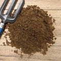 Dandy's Topsoil & Landscape Supplies Rootzone Sand and Soil Mix is shown in a pile on wood beside a metal gardening fork with a blue handle—perfect for improving lawn drainage.